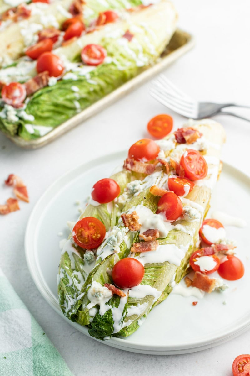 grilled wedge salad on a white plate with more wedge salad in the background