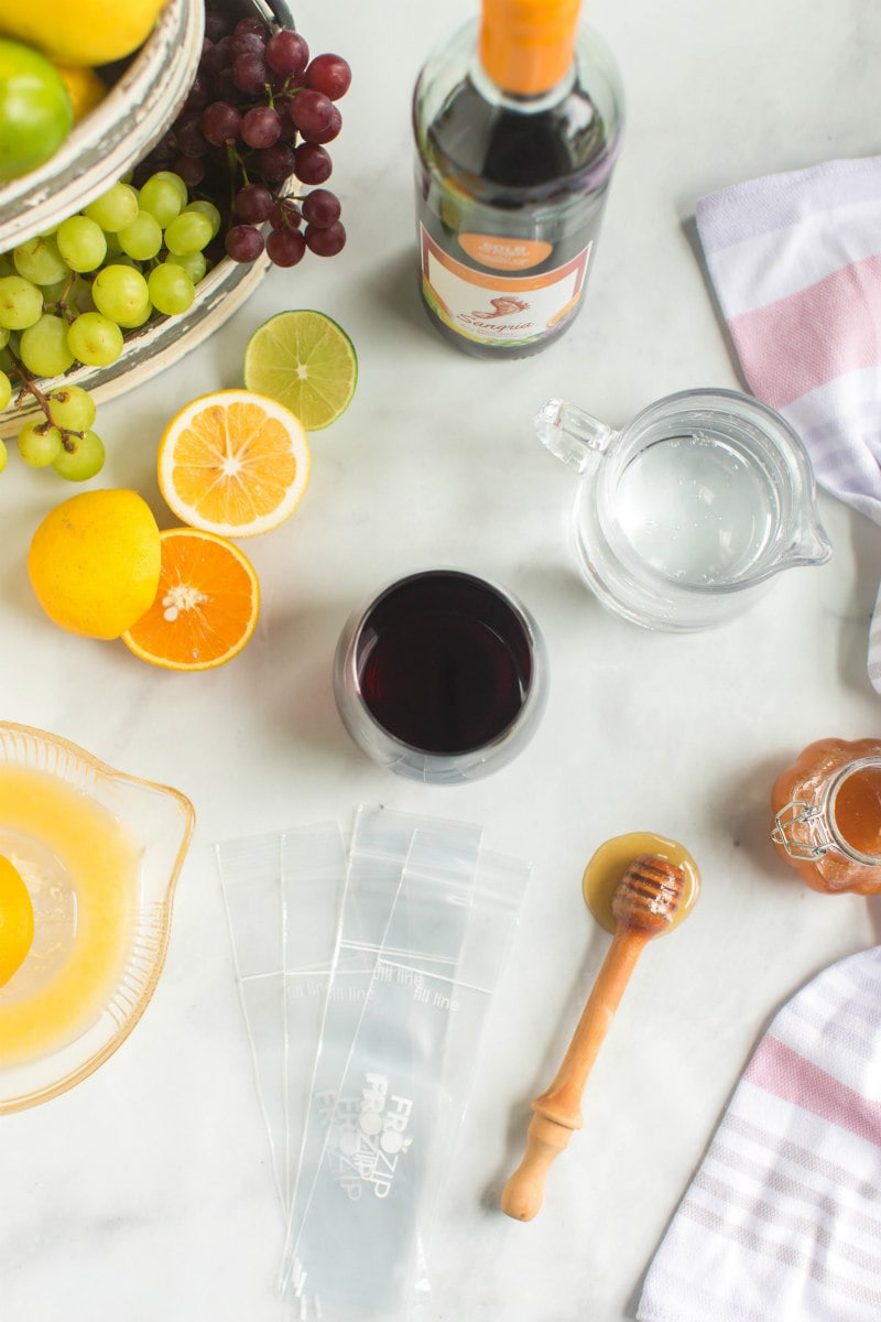 ingredients displayed for making sangria popsicles: sangria, sparking water, lemon, orange and honey