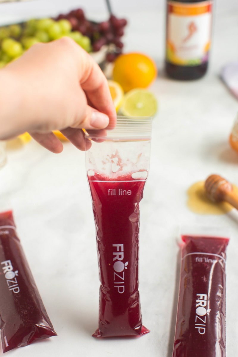 making sangria popsicles- showing the liquid poured into the popsicle wrappers, hand holding one of the wrappers