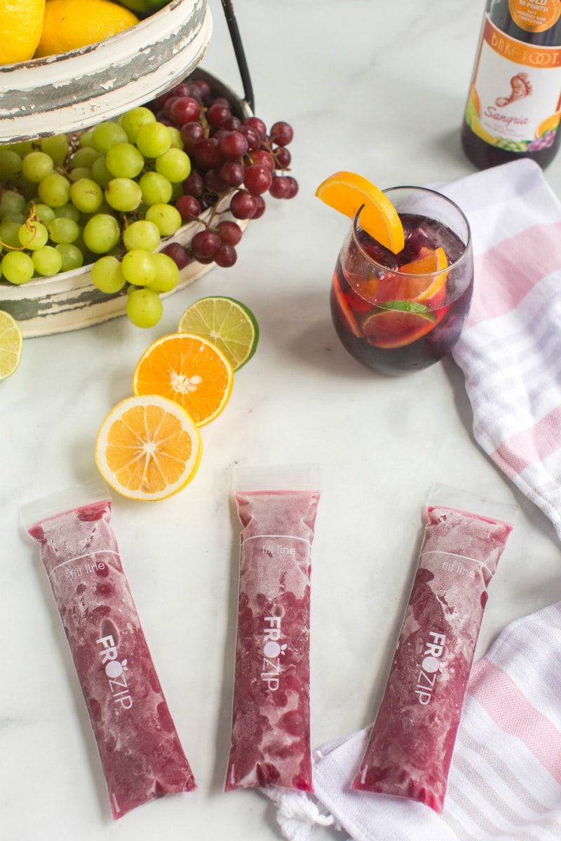 three sangria popsicles with sliced oranges, lemons and grapes and a glass of sangria in the background