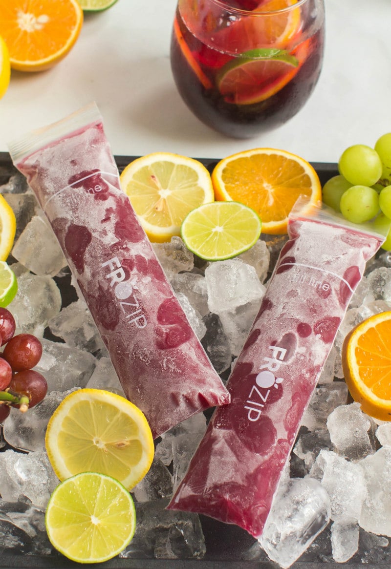 two sangria popsicles set on a tray of ice with sliced oranges, lemons and grapes and a glass of sangria in the background