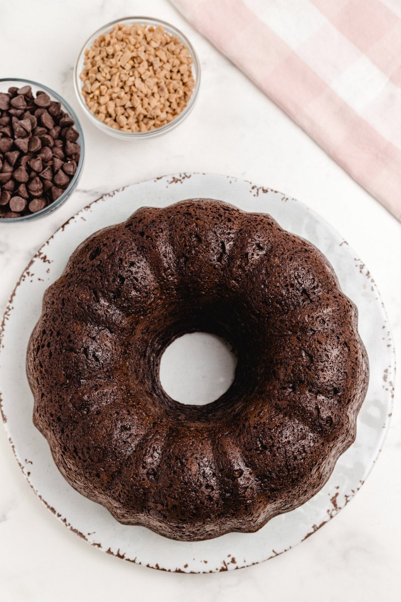 chocolate bundt cake on a white platter. chocolate chips and toffee chips in bowls on the side