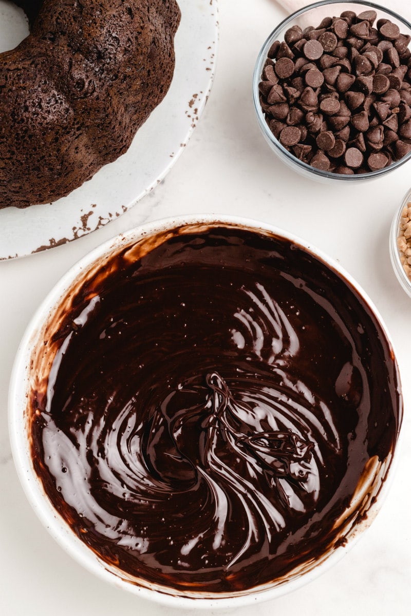 chocolate ganache in a white bowl. chocolate cake and bowl of chocolate chips on the side