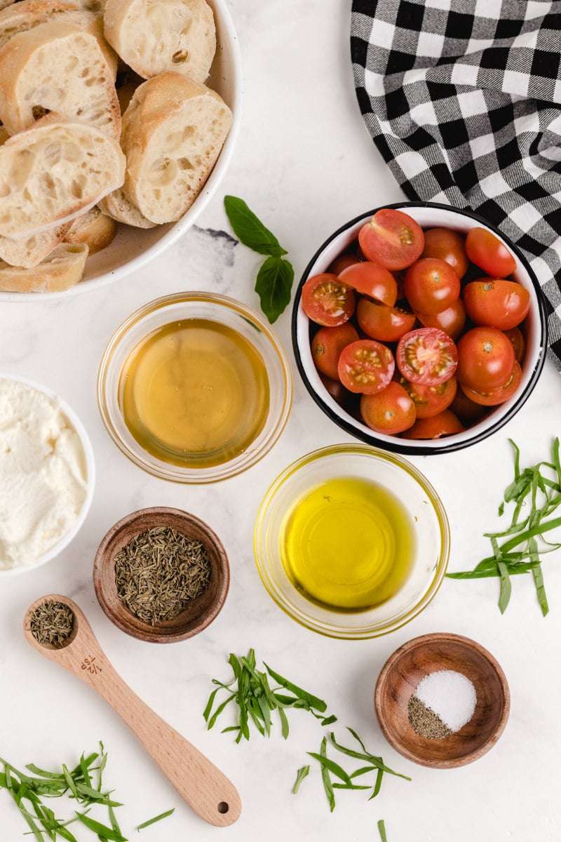 overhead shot of ingredients for honey tomato bruschetta in bowls: baguette slices, tomatoes, oil, ricotta, spices