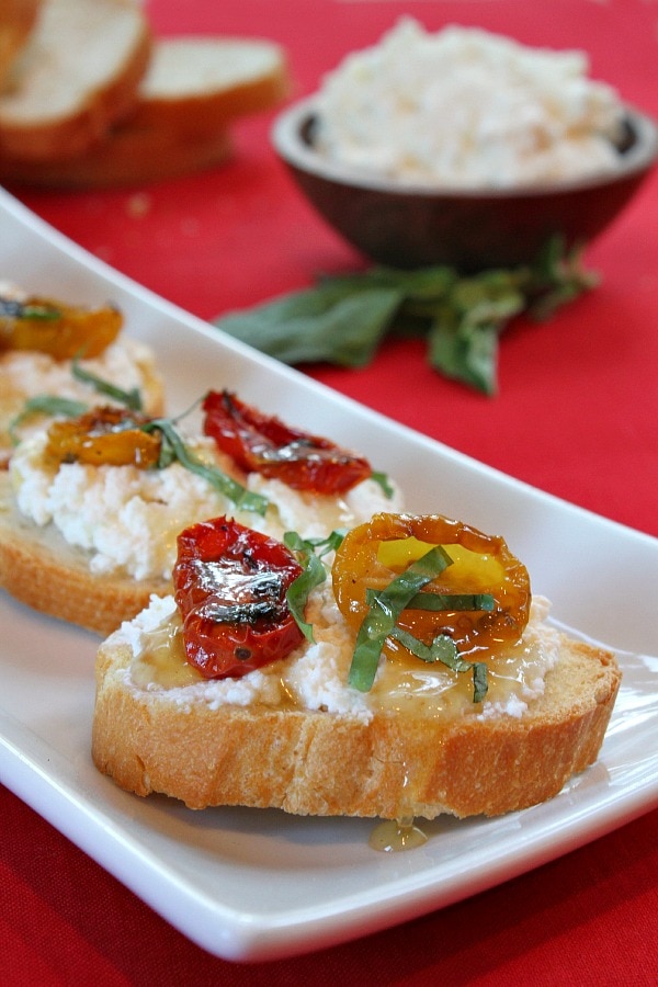 honey tomato bruschetta displayed on a white plate with fresh basil leaves on a red background