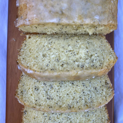 overhead shot of glazed lemon poppy seed bread cut into slices on a wood board