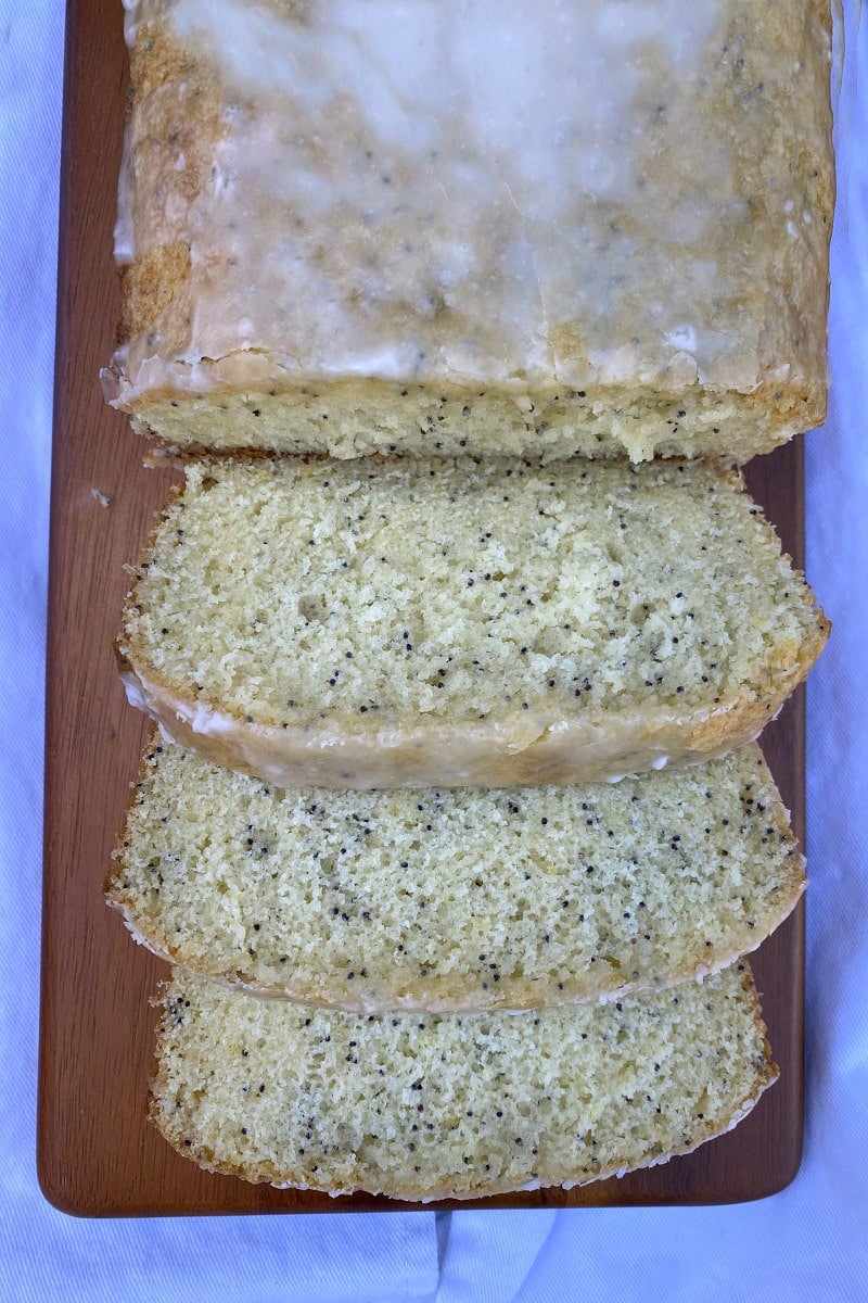 overhead shot of glazed lemon poppy seed bread cut into slices on a wood board