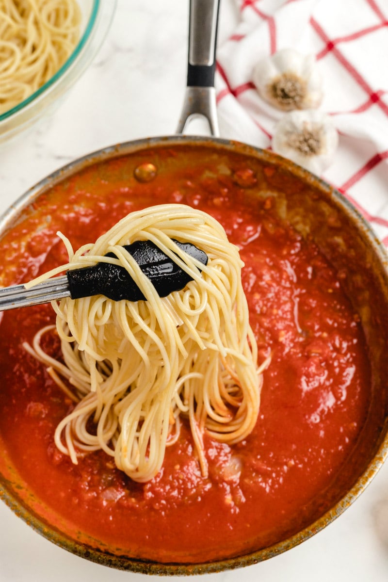 adding pasta to red sauce in a skillet