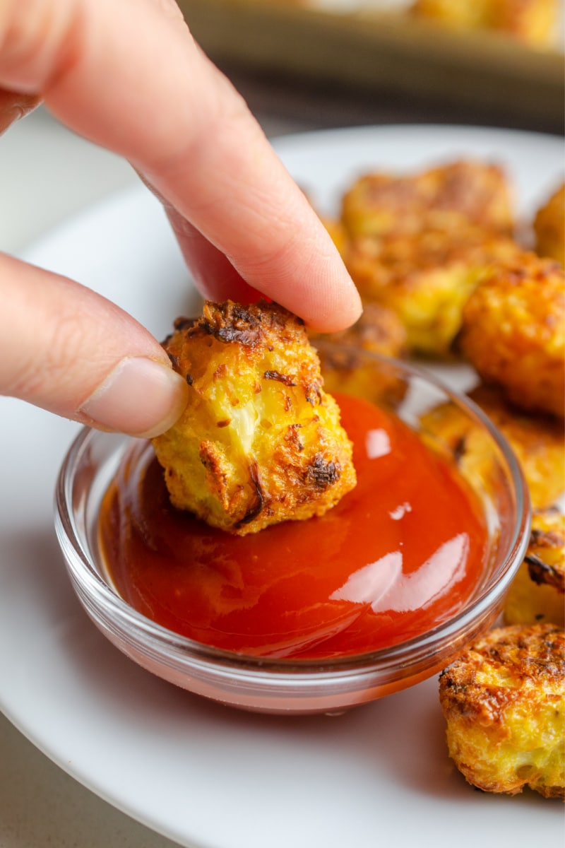 hand dipping cauli tot into ketchup