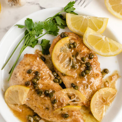 chicken piccata on a white plate with lemon and parsley