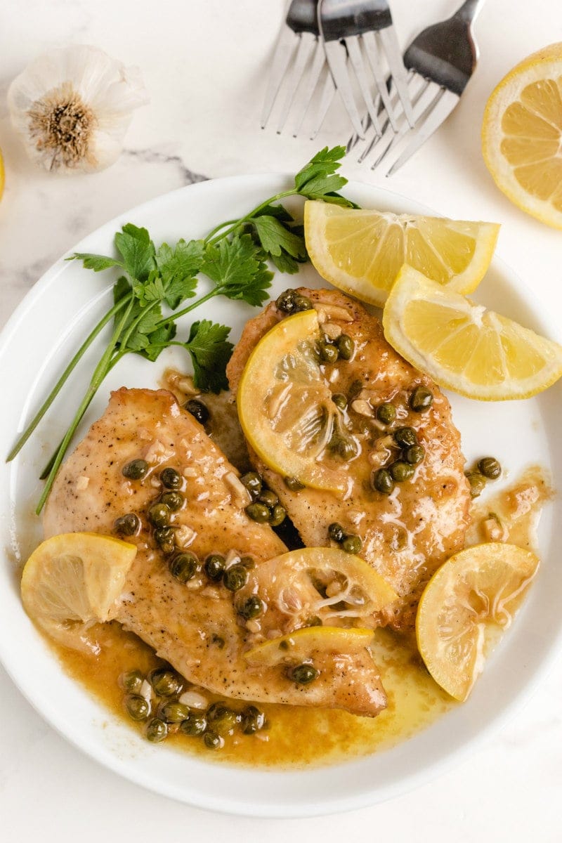 chicken piccata on a white plate with lemon and parsley