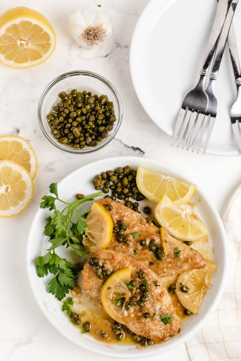 chicken piccata on a white plate with capers and lemons