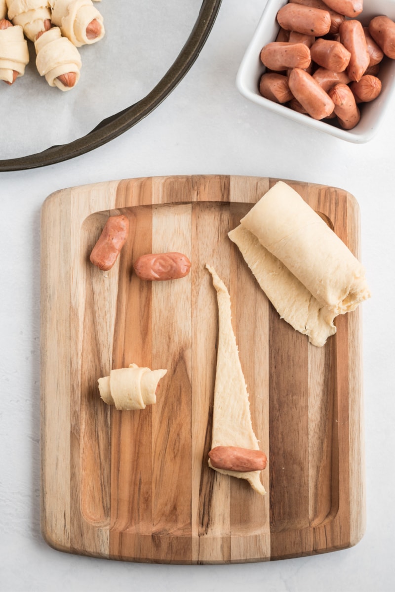 showing process of making pigs in blanket rolling up pigs in crescent dough on board