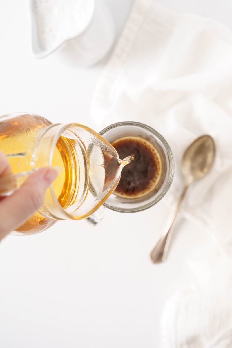 pouring vanilla syrup into coffee in mug