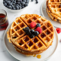 stack of waffles on plate topped with fruit and syrup