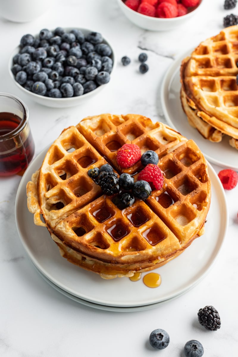 stack of waffles on plate topped with fruit and syrup