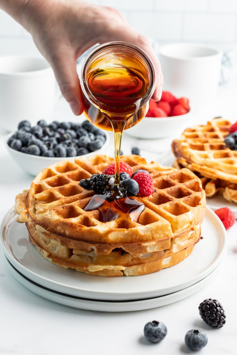 pouring syrup onto stack of greek yogurt waffles with fruit on top