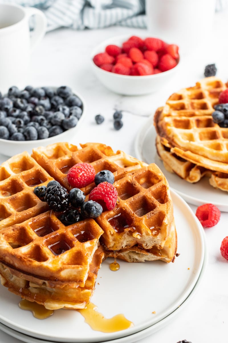 stack of waffles on plate with piece cut out topped with fruit