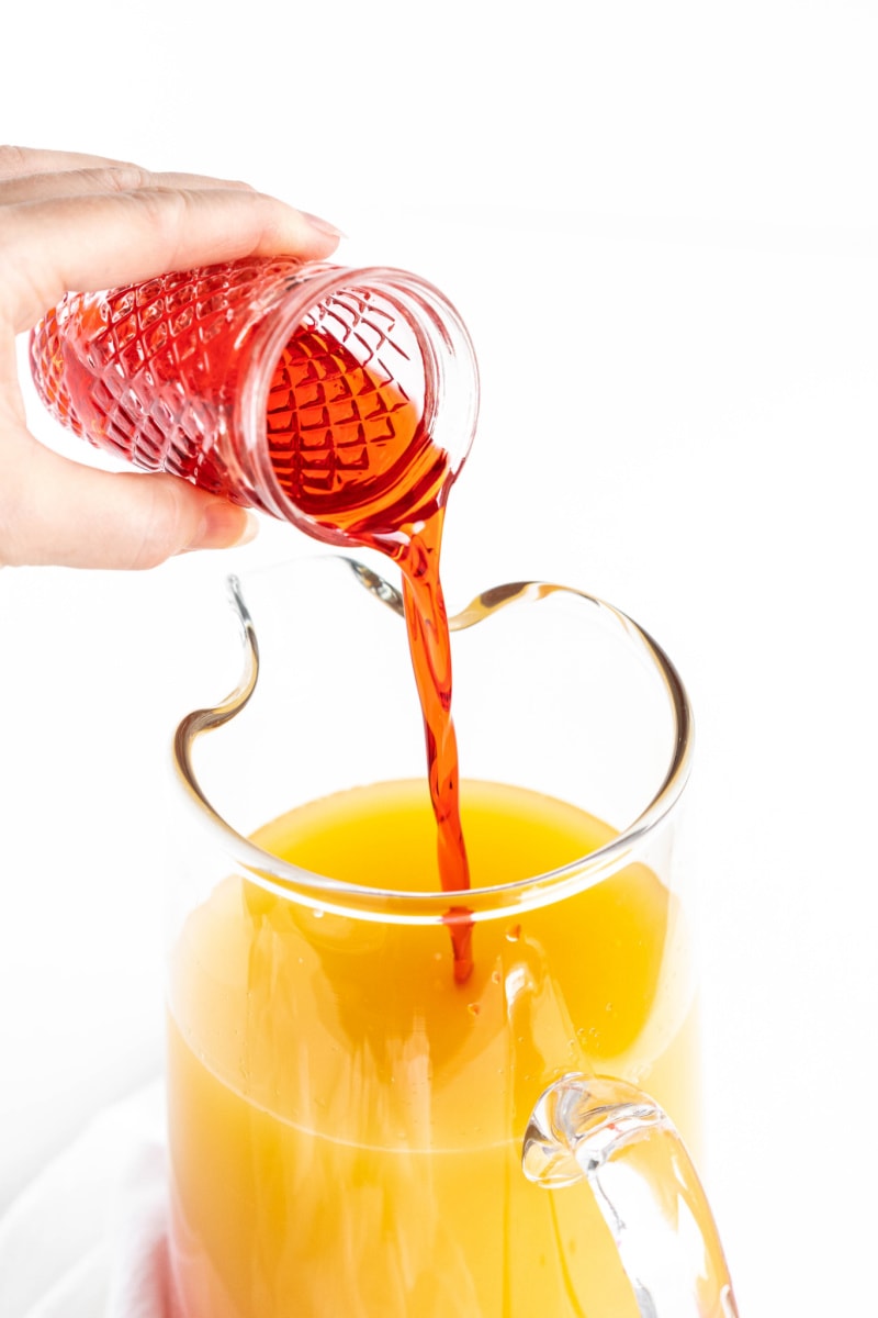 pouring grenadine into pitcher with juices