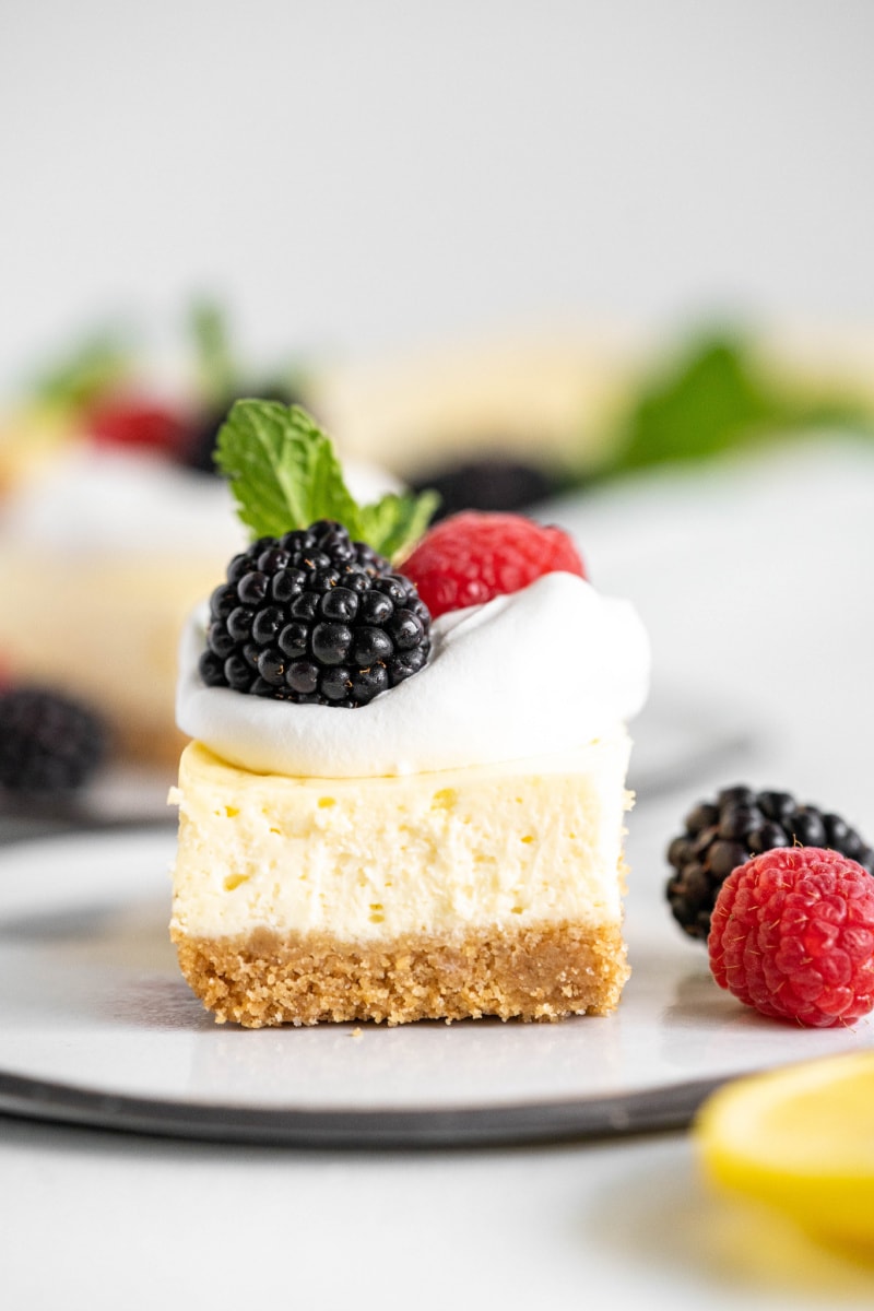 lemon cheesecake bar topped with whipped cream and berries