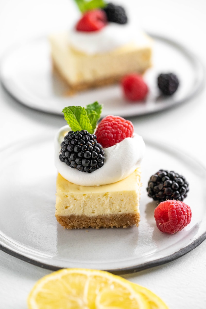 lemon cheesecake bar on white plate topped with whipped cream and berries