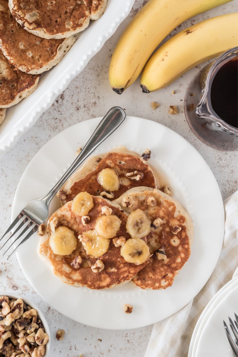 overhead shot of three pancakes with bananas on top on white plate