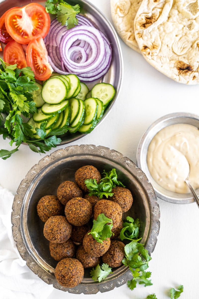 falafel in bowl with bowl of tahini sauce and fresh veggies and flatbread