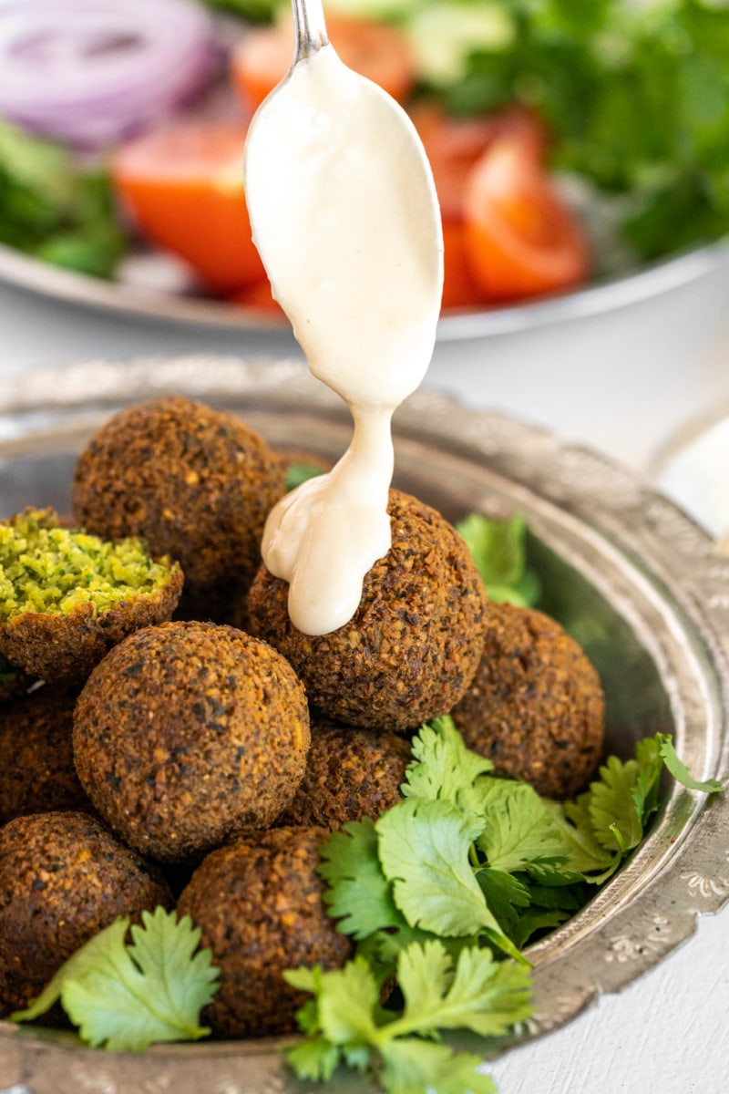 tahini sauce being drizzled onto falafel in bowl