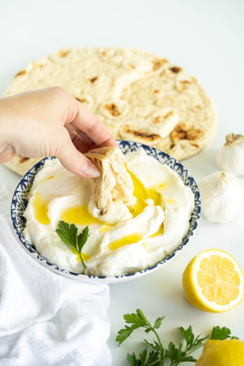 dipping pita into garlic sauce in a bowl