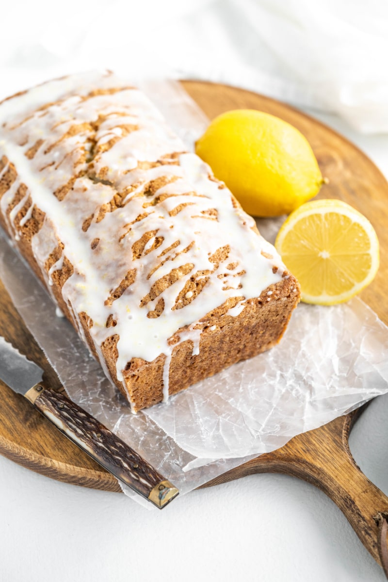 loaf of iced lemon zucchini bread on cutting board with lemons