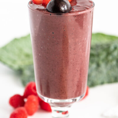 berry detox smoothie in a tall glass with fresh fruit garnishes