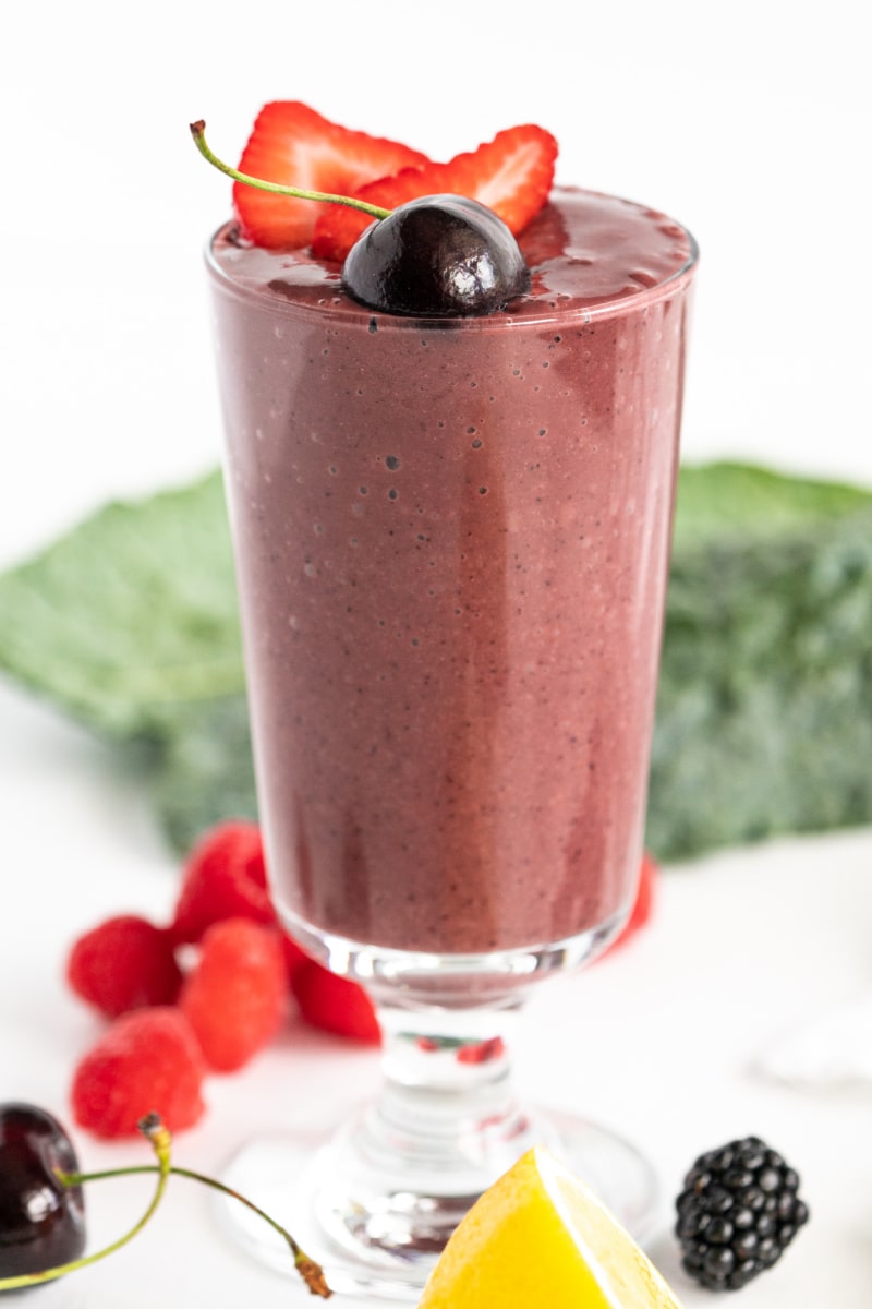 berry detox smoothie in a tall glass with fresh fruit garnishes