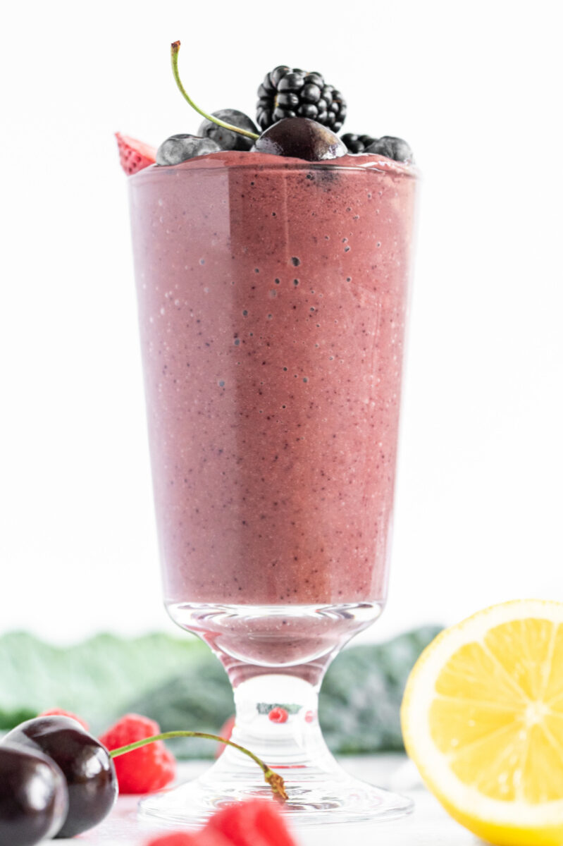 berry detox smoothie in a tall glass with fresh fruit garnishes