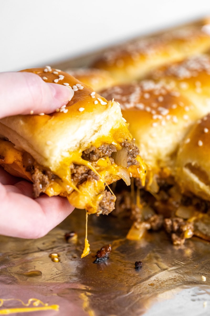 hand pulling a cheeseburger slider out of a pan