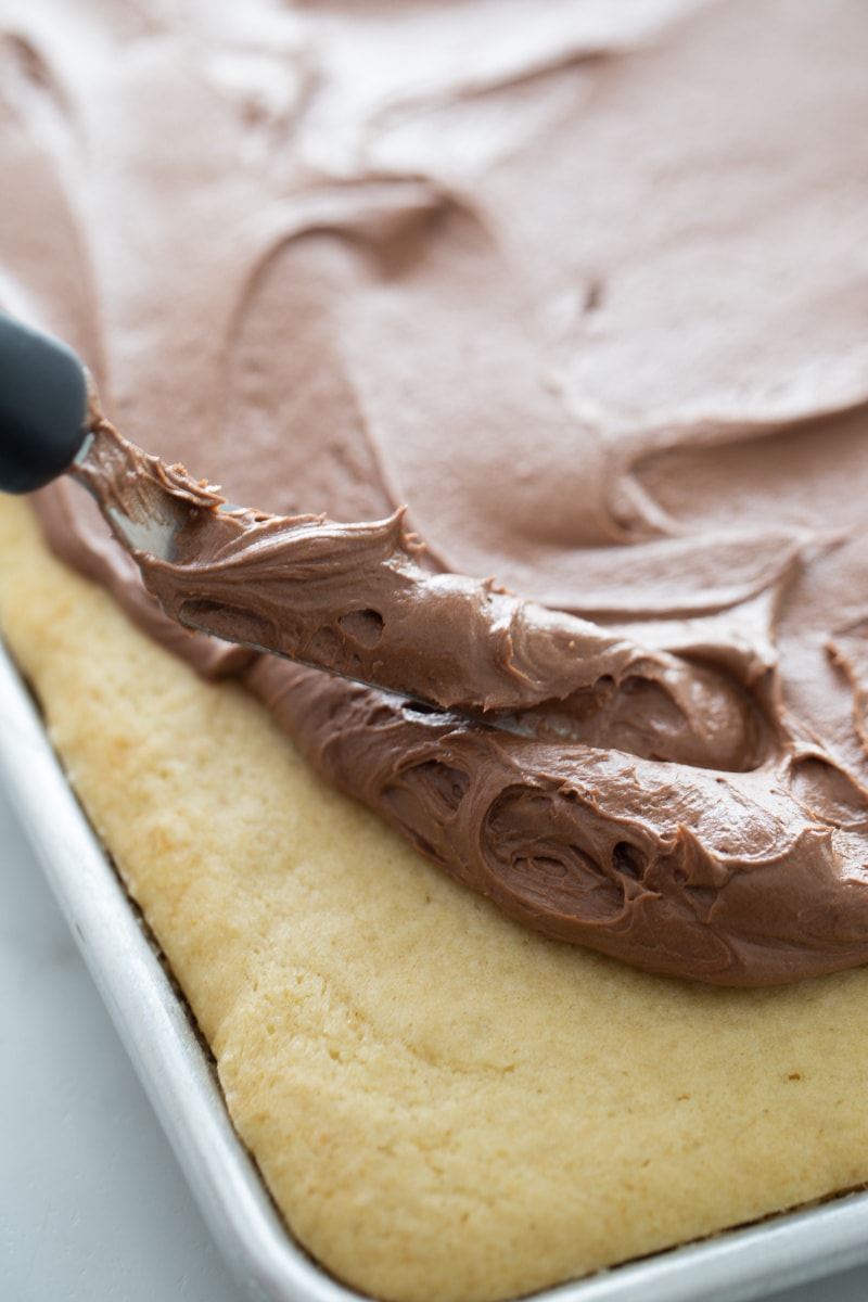 yellow sheet cake being frosted with chocolate frosting