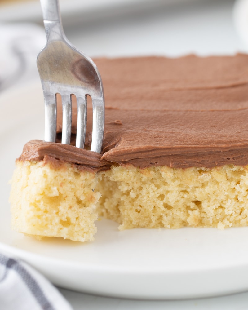 fork taking bite of yellow cake with chocolate frosting