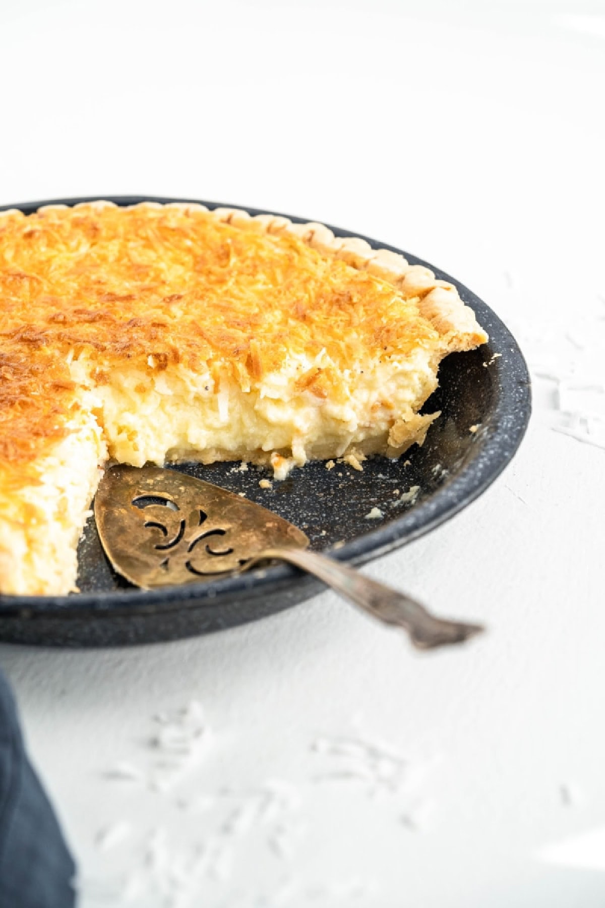 This Old Fashioned Coconut Custard Pie is rich, creamy and packed with sweet coconut flavor! 🥥 Made with a silky homemade custard and flaky pie crust, it's the perfect dessert for Thanksgiving, Easter, Christmas or Sunday dinner. Save this classic pie recipe! #coconutcustardpie #pierecipes #dessertrecipes #oldfashionedrecipes #holidaydesserts coconut custard pie with big slice taken out of it