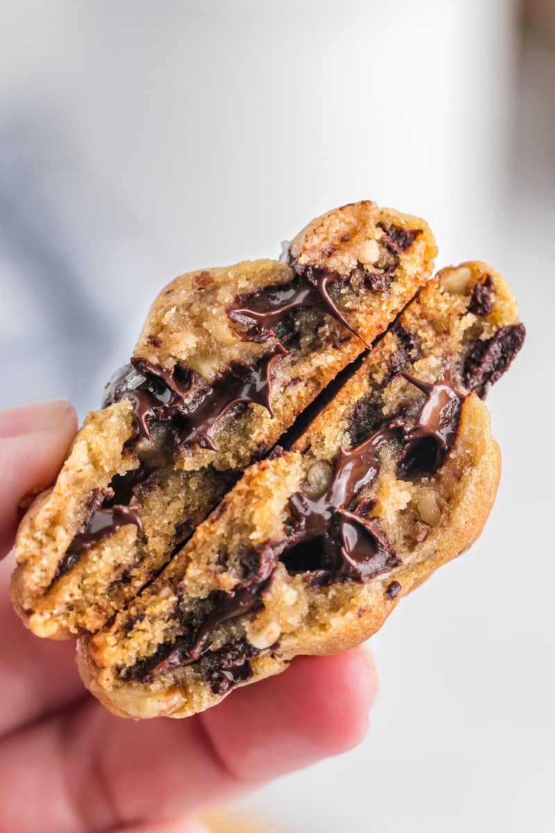 hand holding warm chocolate chip cookie snapped in half to show gooey inside