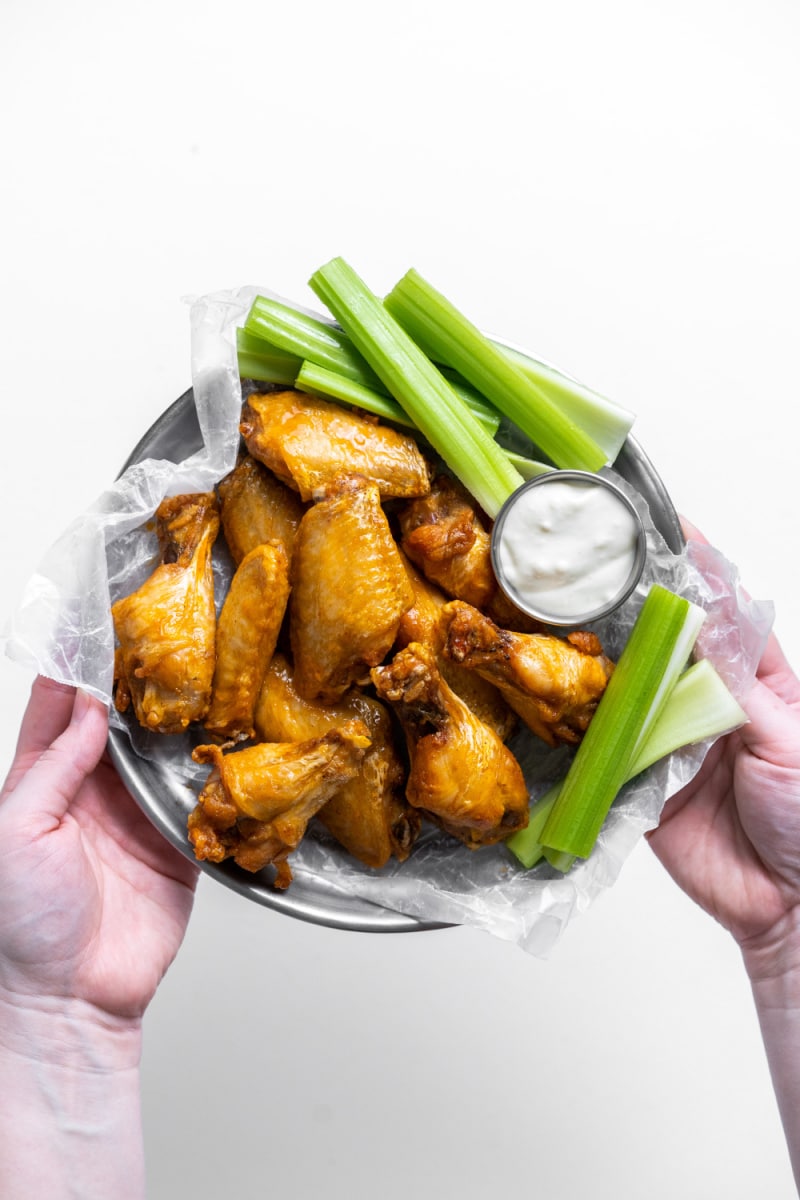 hands holding plate of buffalo wings with celery and blue cheese dressing