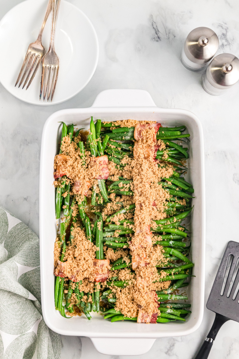bacon wrapped green beans in a baking dish with brown sugar sprinkled on top