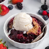 berry crumble in a white dish with a scoop of vanilla ice cream on top