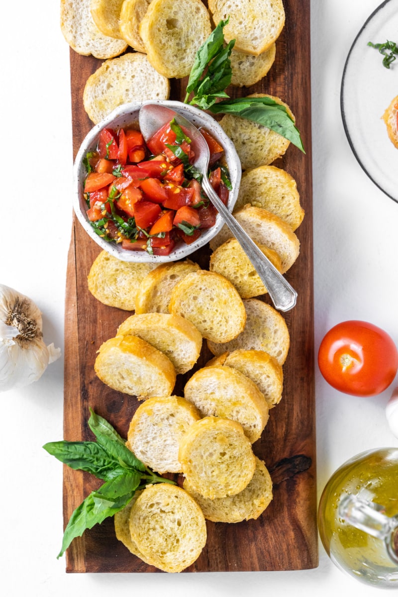 board with toasted baguette and bowl of bruschetta spread