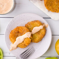 two fried green tomatoes on a plate topped with remoulade sauce