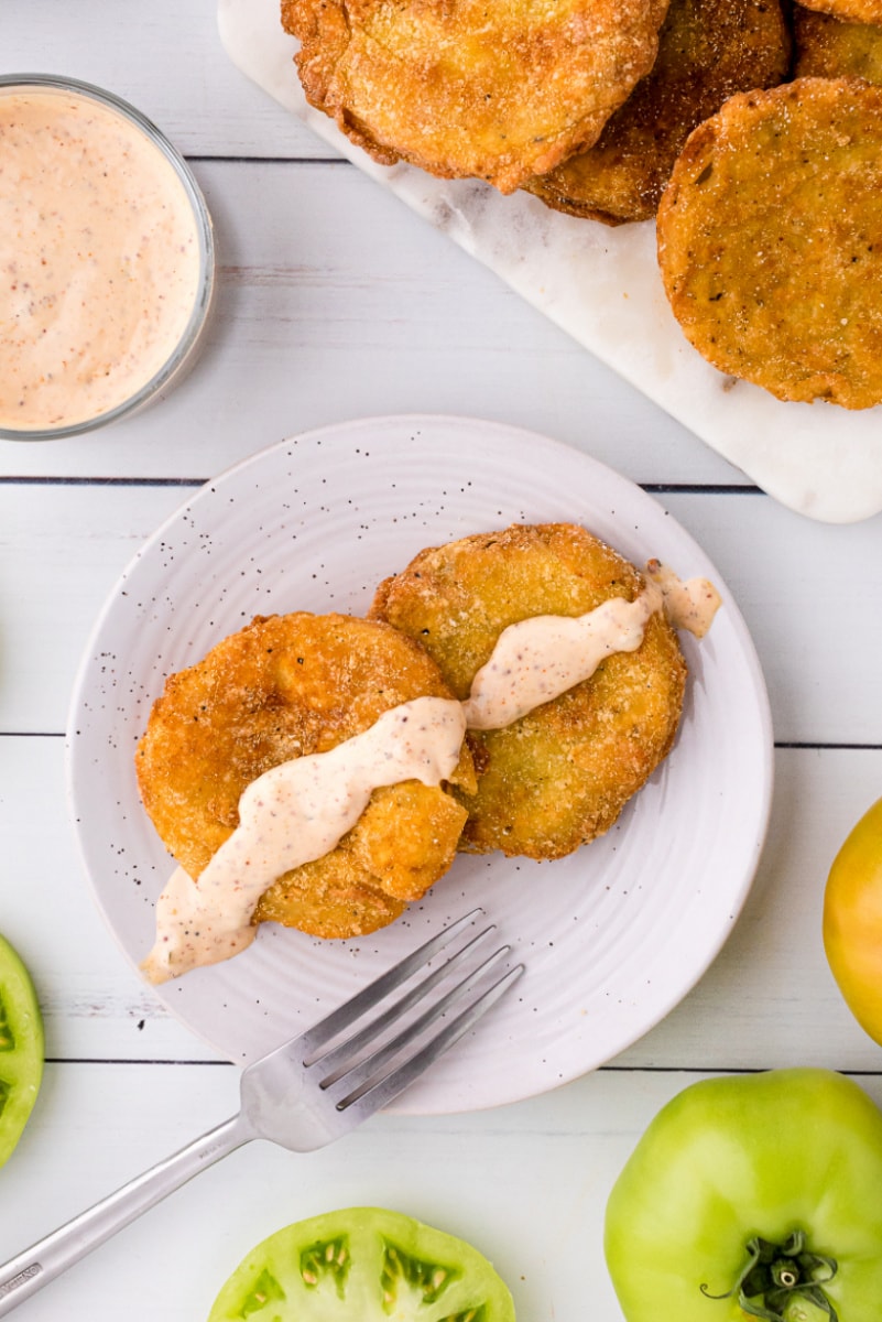 two fried green tomatoes on a plate topped with remoulade sauce
