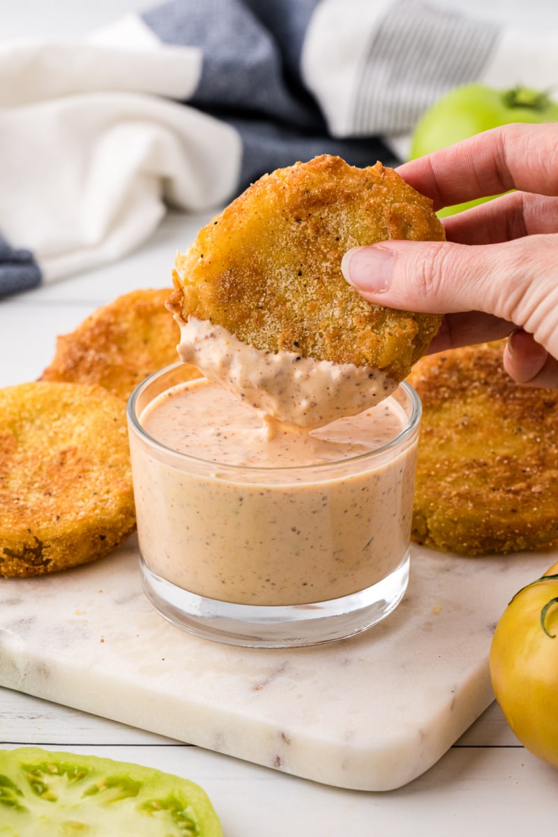 dipping fried green tomato into jar of remoulade sauce