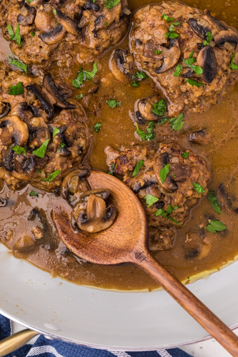 salisbury steak in a skillet with a wooden spoon