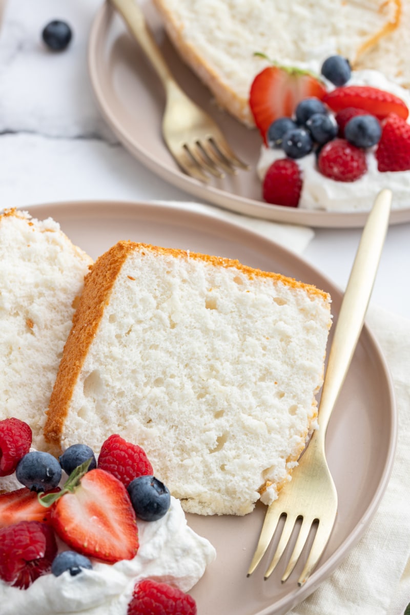 slices of angel food cake on plate with fork and whipped cream and berries