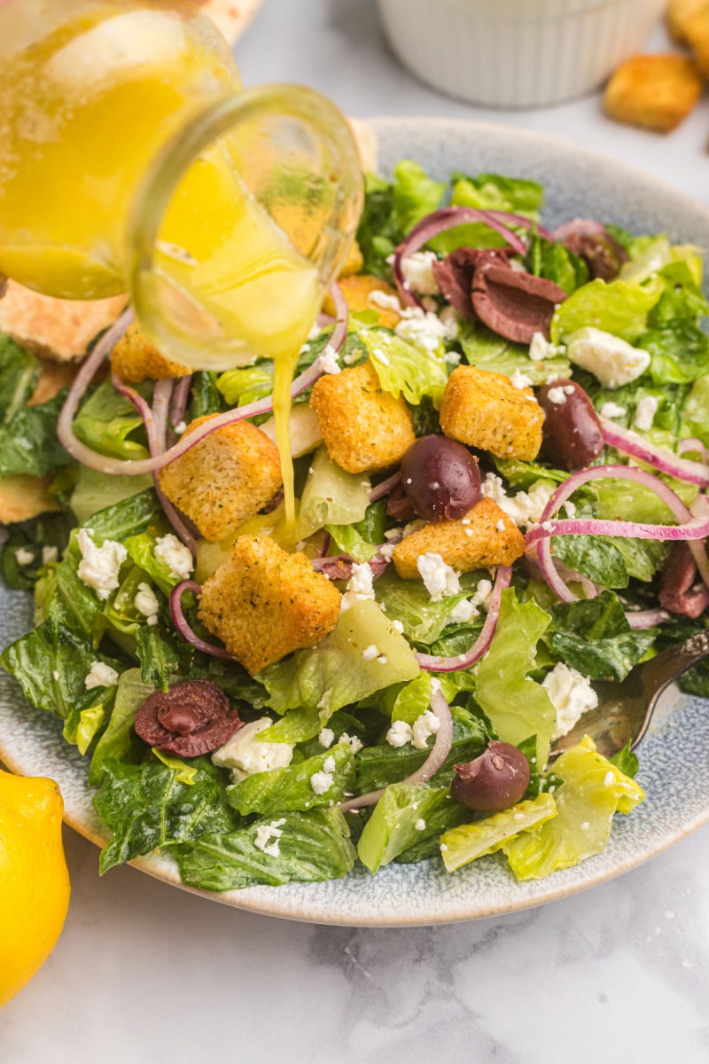 pouring salad dressing onto salad on plate