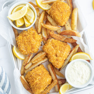 baked fish and chips in pan with lemon wedges and sauce