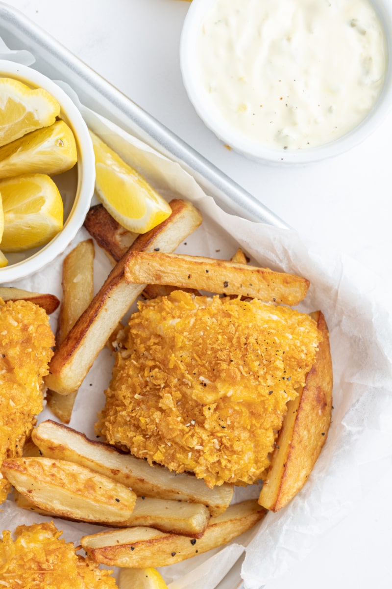 baked fish and chips on a pan with lemon wedges and sauce on side